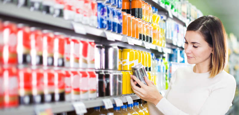 Femme tenant une cannette de soda dans un supermarché - taxe soda