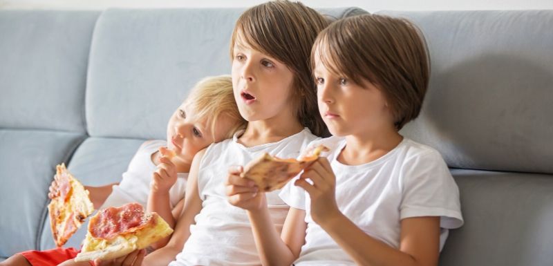 3 enfants assis sur le canapé en mangeant de la pizza