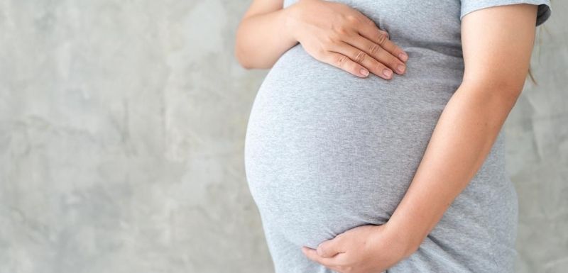 Femme enceinte habillée d'une robe grise tenant son ventre entre ses deux mains